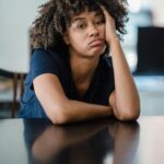 A portrait of a woman looking bored with her head resting on a table indoors.