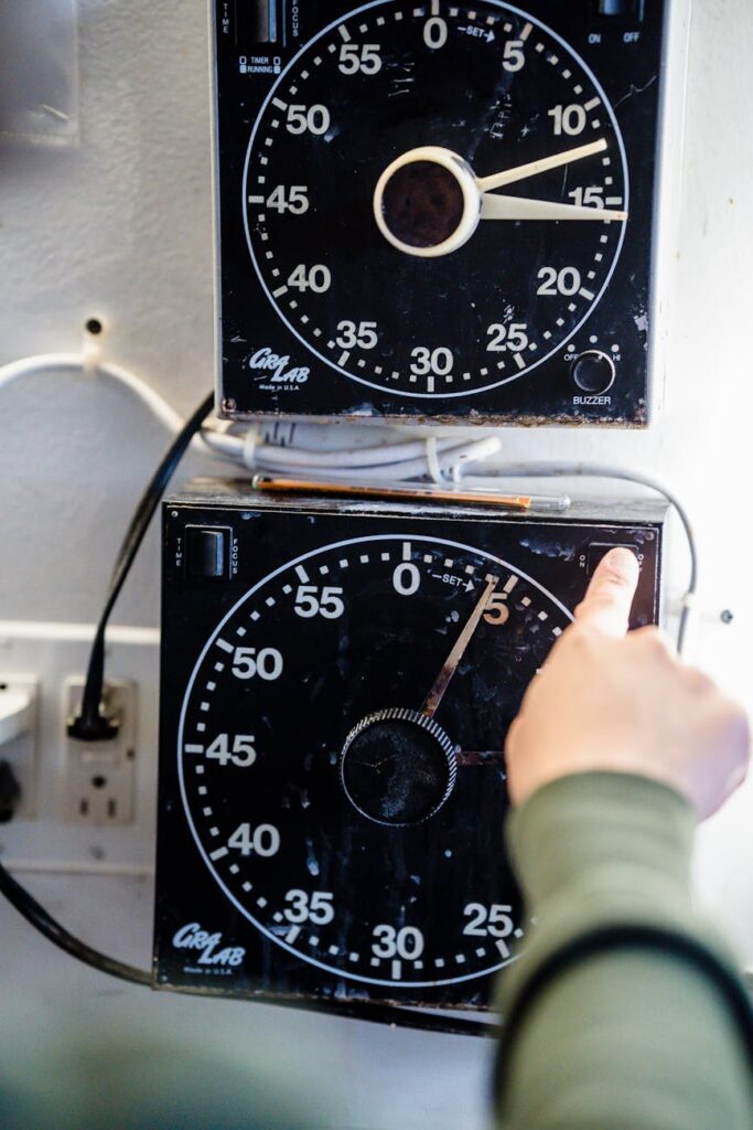 A hand adjusting an industrial analog timer on a wall. Focus on mechanical functionality and precision.